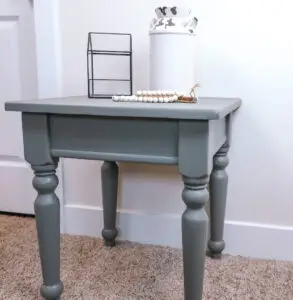Thrifted Small side table, sanded, stained grey against wall. White chipped pitcher, glass house terrarium, wooden beads, wooden coaster on top.