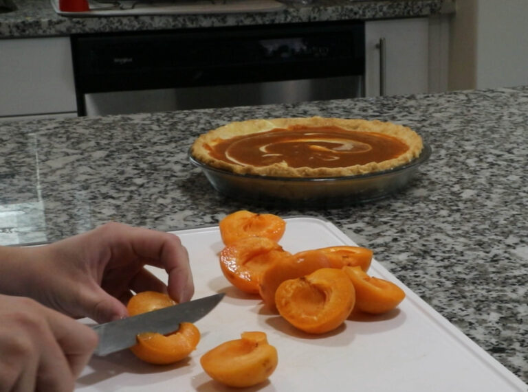 Cutting apricots on cutting board. Pie in the background.