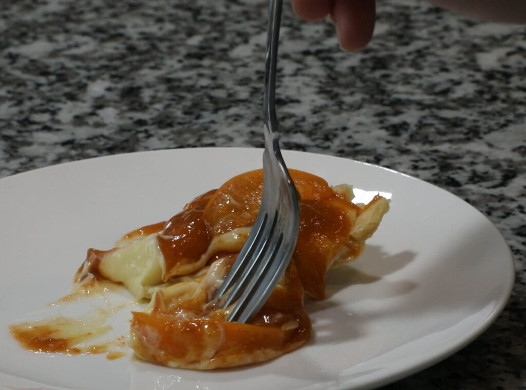 Fork piercing apricot with pie and plate in the background.