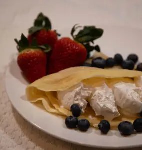 Homemade sourdough crepes with whipped cream, blueberries, and strawberries