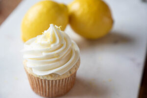 Frosted and zested lemon cupcakes on marble with lemons in the background