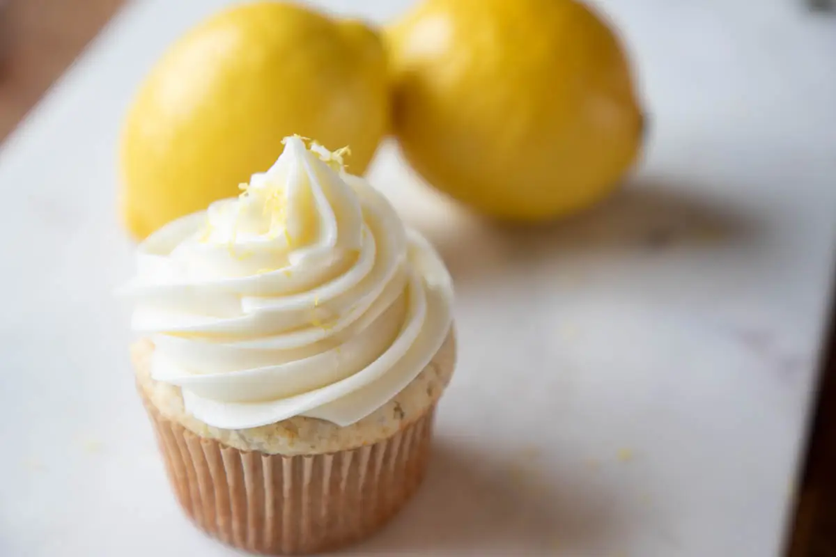 Frosted and zested lemon cupcakes on marble with lemons in the background