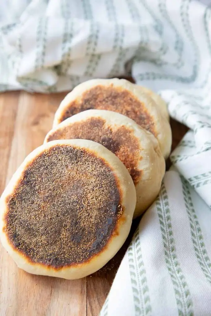English muffins stacked on each other. Sitting on wooden cutting board with green fabric.