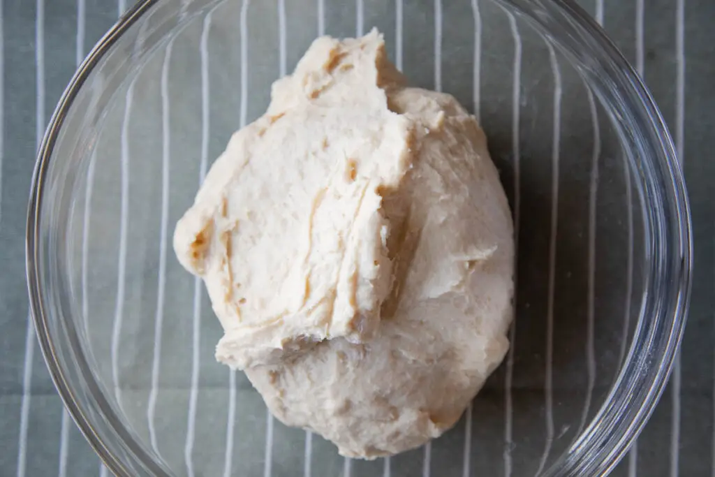 Sourdough english muffin dough in glass bowl on green fabric