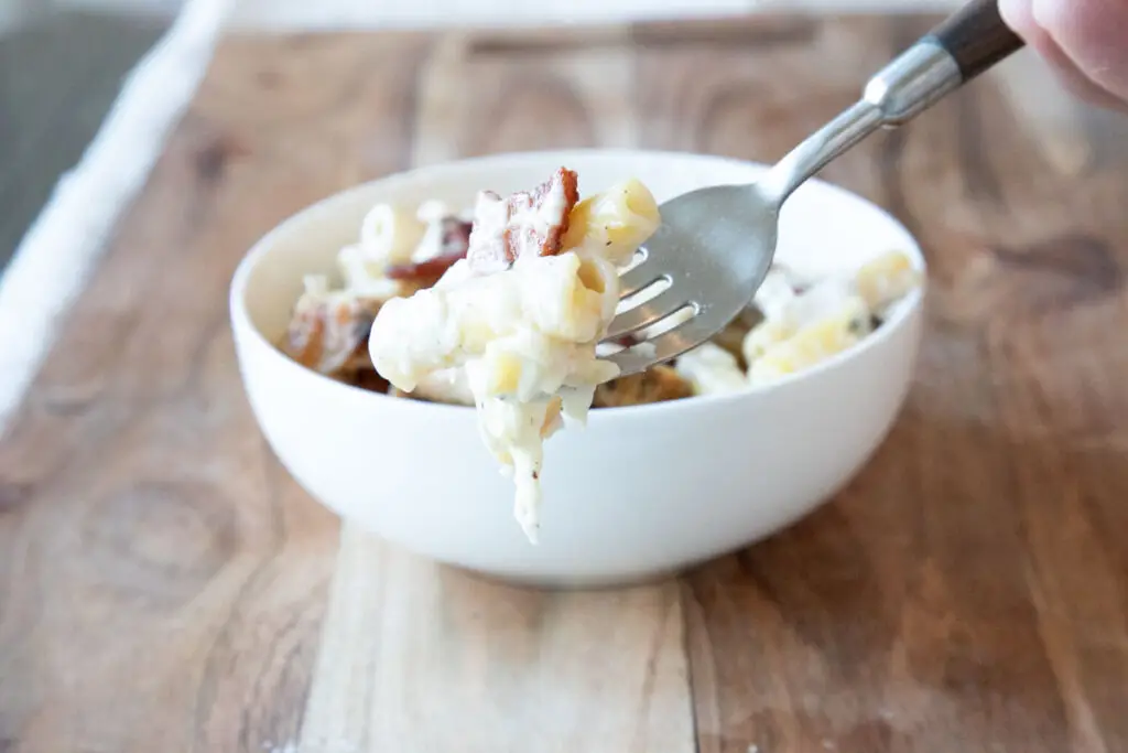 Chicken alfredo baked ziti in white dish on wooden board with fork holding a bite