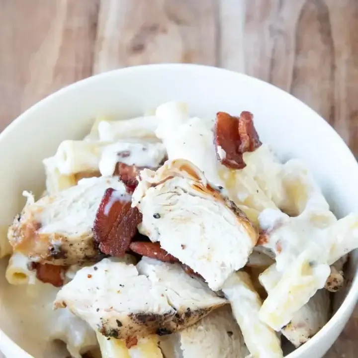 Chicken alfredo baked ziti in white dish on wooden board